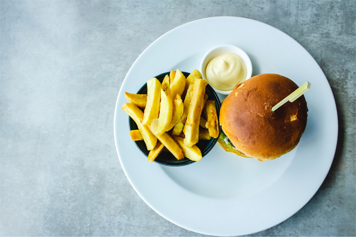 Burger with fries and sauce on a white plate, gray surface.