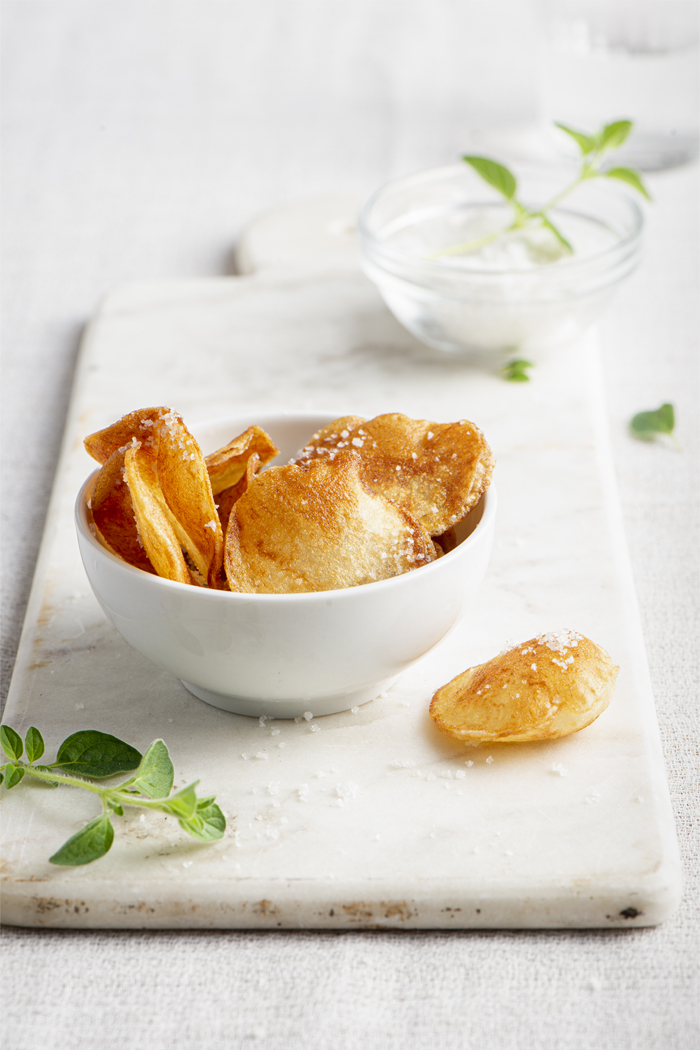 Chips in a white bowl on a marble board. Fresh herbs and salt are also present.