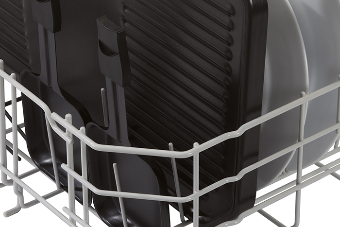 Close-up of a dishwasher rack holding black grill pans and white plates. The rack is white metal.