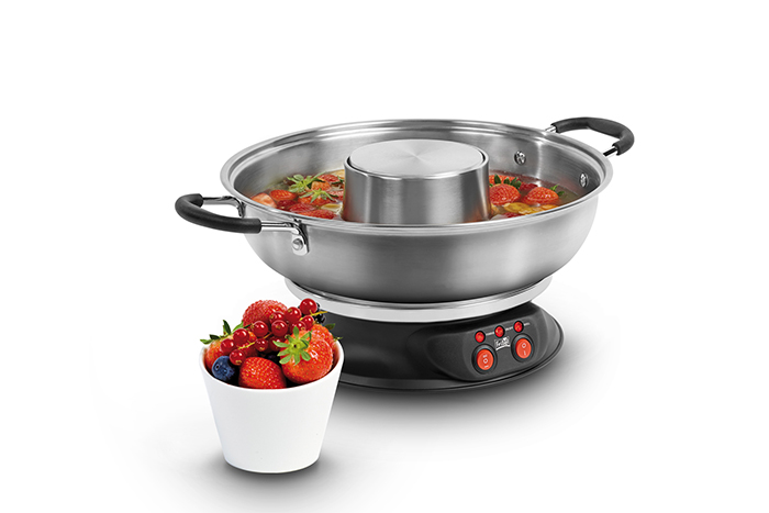 Een roestvrijstalen fonduepan met een witte kom gevuld met aardbeien.