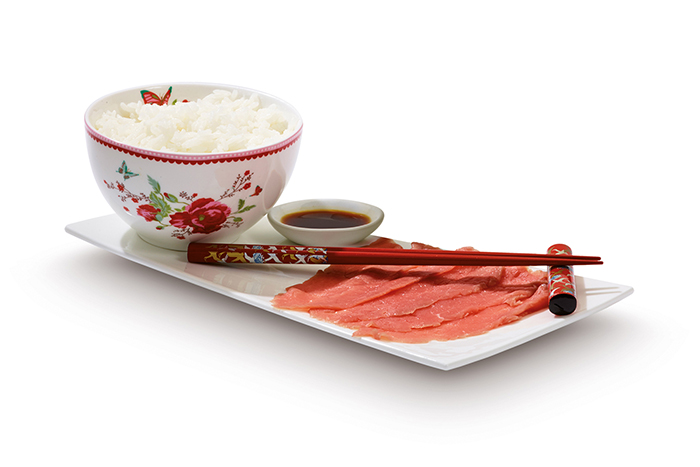 Plate with rice, soy sauce, and sliced meat with chopsticks.