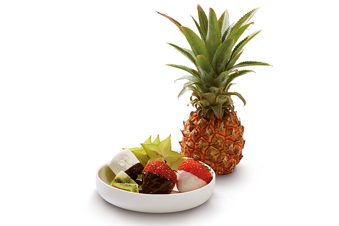 A bowl of chocolate-covered strawberries, kiwi, and starfruit. A pineapple is behind.