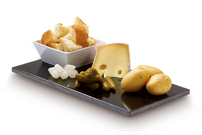 A platter of food: cheese, bread, pickles, and potatoes on a black surface.