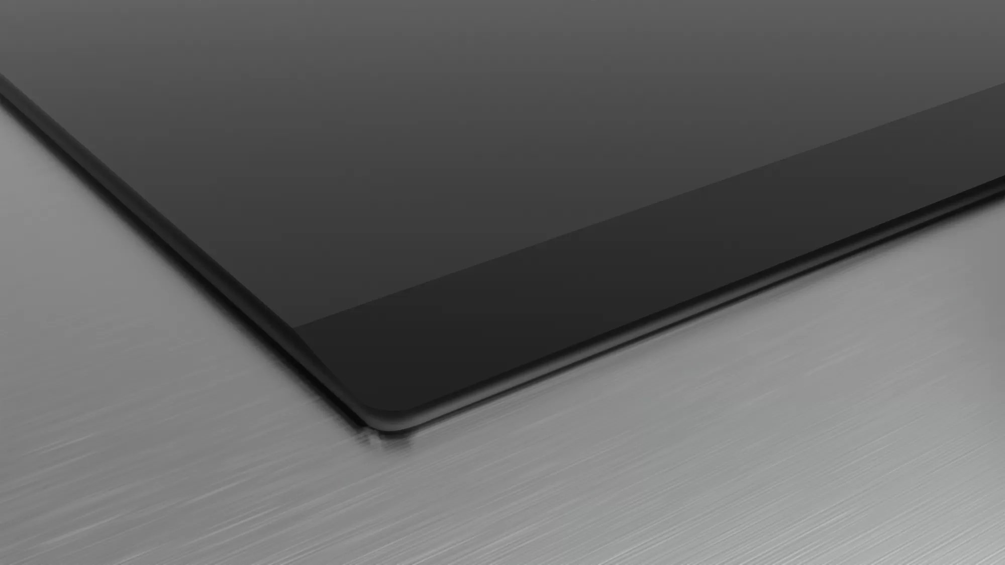 Close-up of a black glass cooktop on a brushed metal surface, showing a corner.