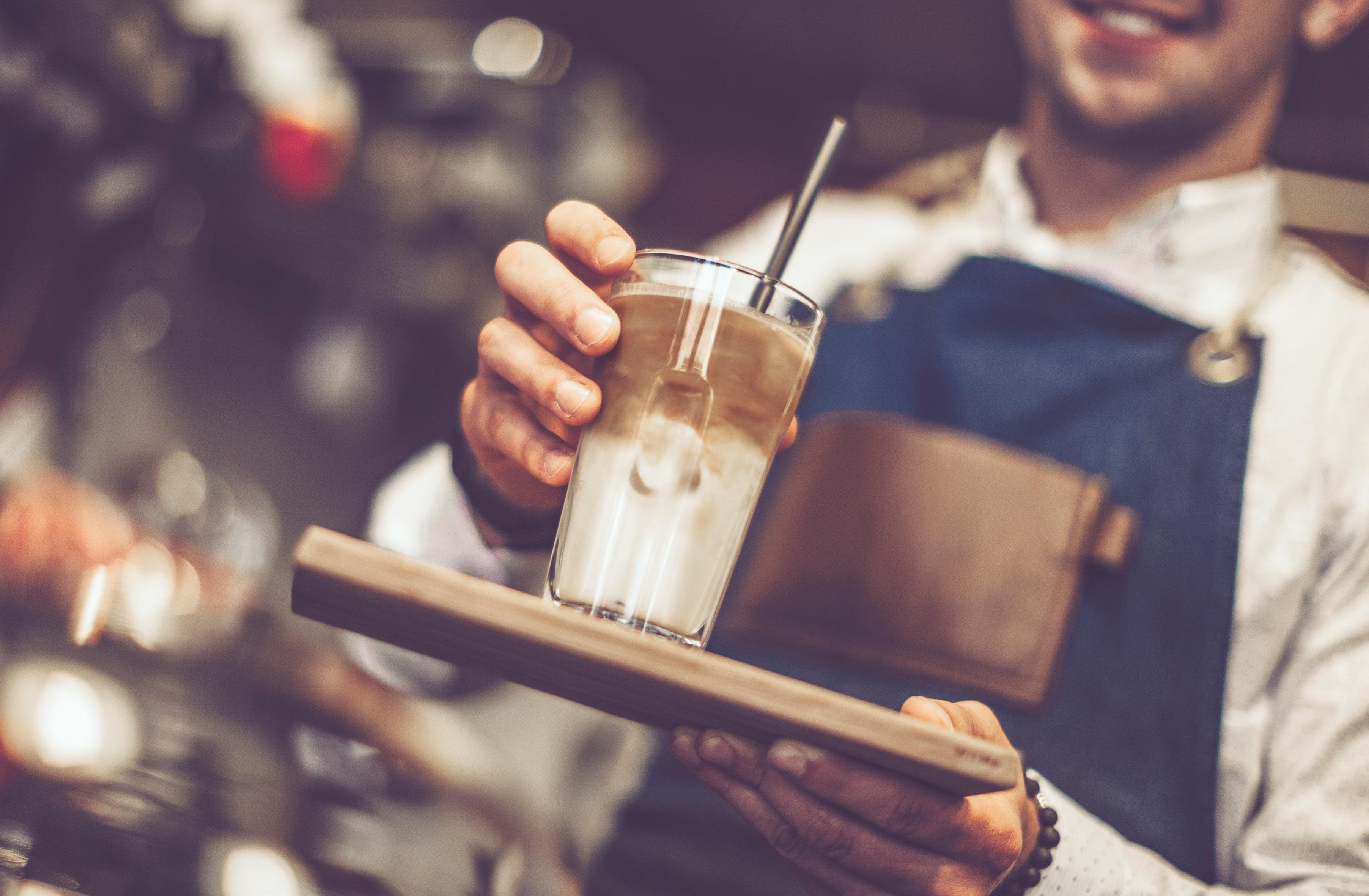 Ein Barkeeper hält ein Tablett mit einem Glas geschichteten Kaffeegetränks.