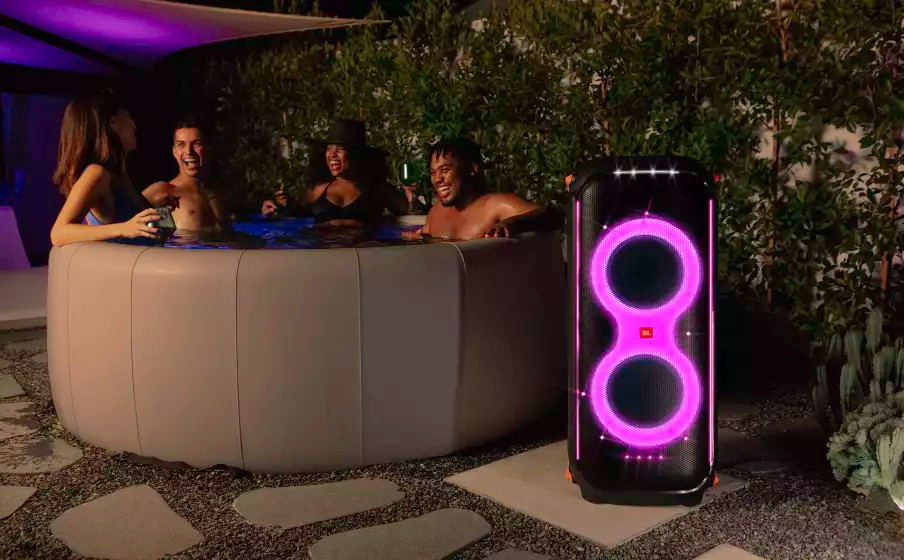 Mensen genieten van een feestje in een jacuzzi met een JBL-luidspreker aan de zijkant 's nachts.