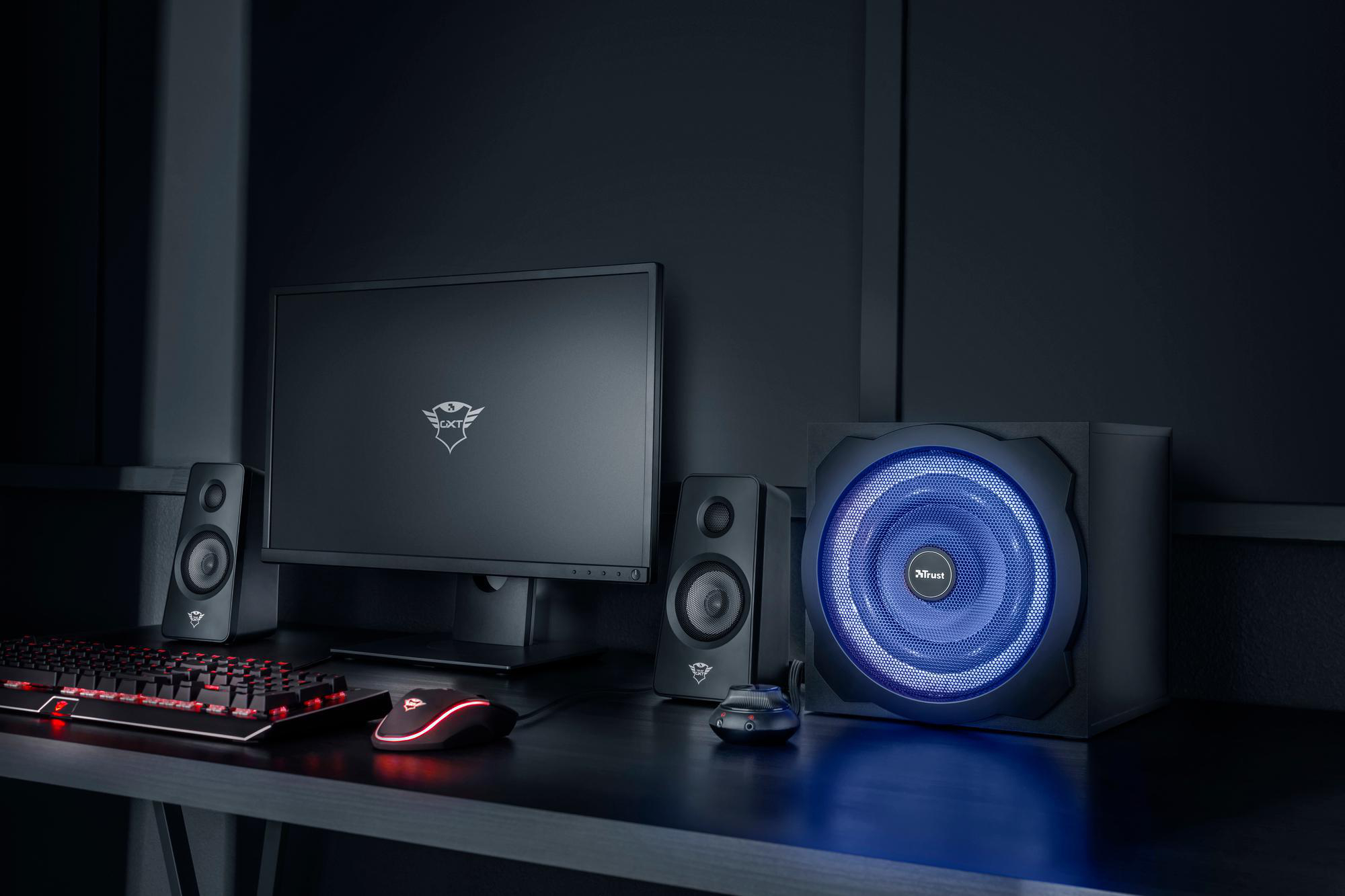 Ein Gaming-Setup mit Monitor, Lautsprechern, Tastatur und Maus. Der Raum ist dunkel.