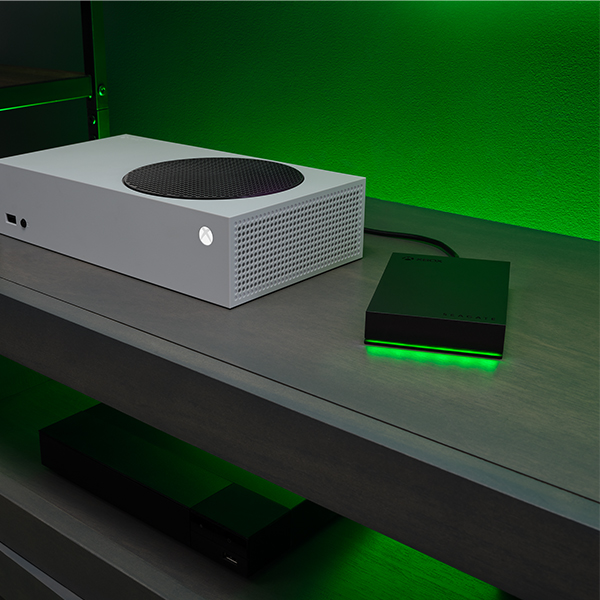 White Xbox Series S, black external hard drive, green lighting.