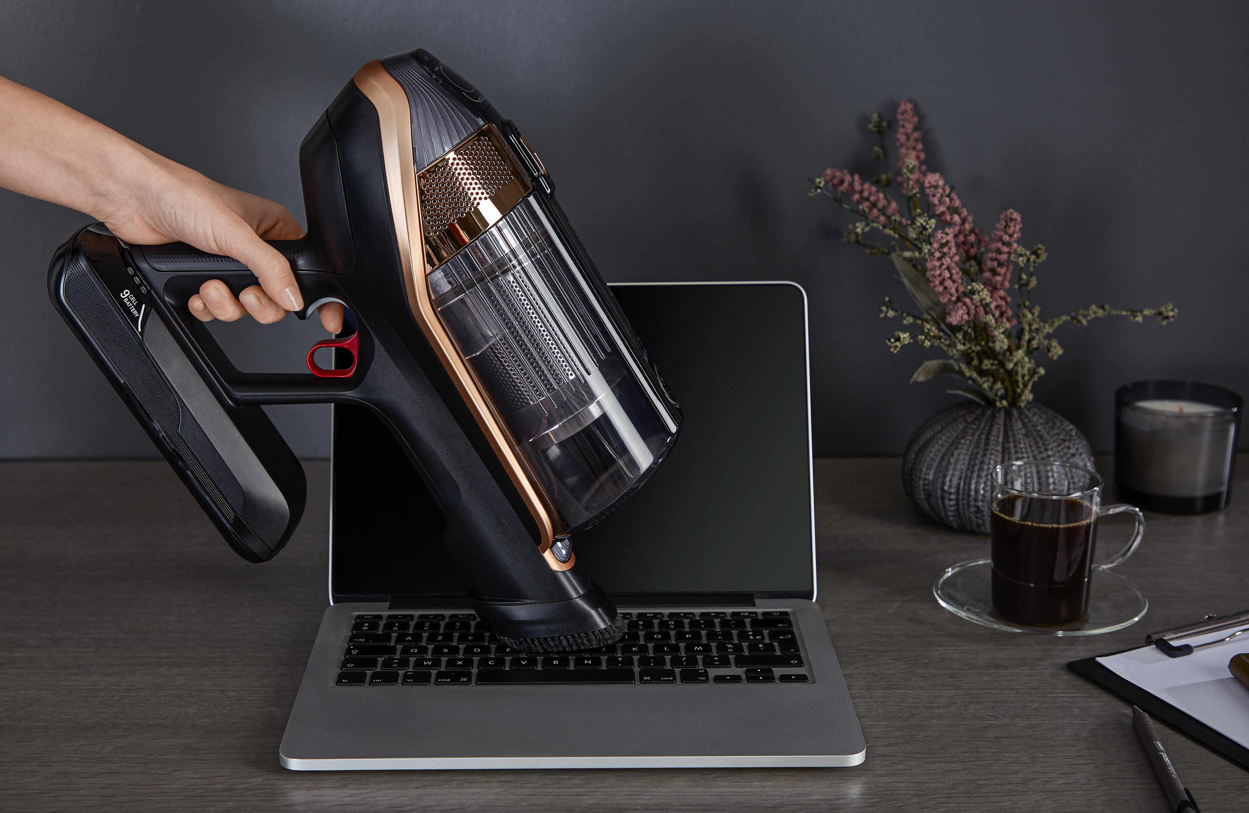 Hand, die einen schwarz-goldenen Staubsauger auf einer Laptop-Tastatur verwendet.