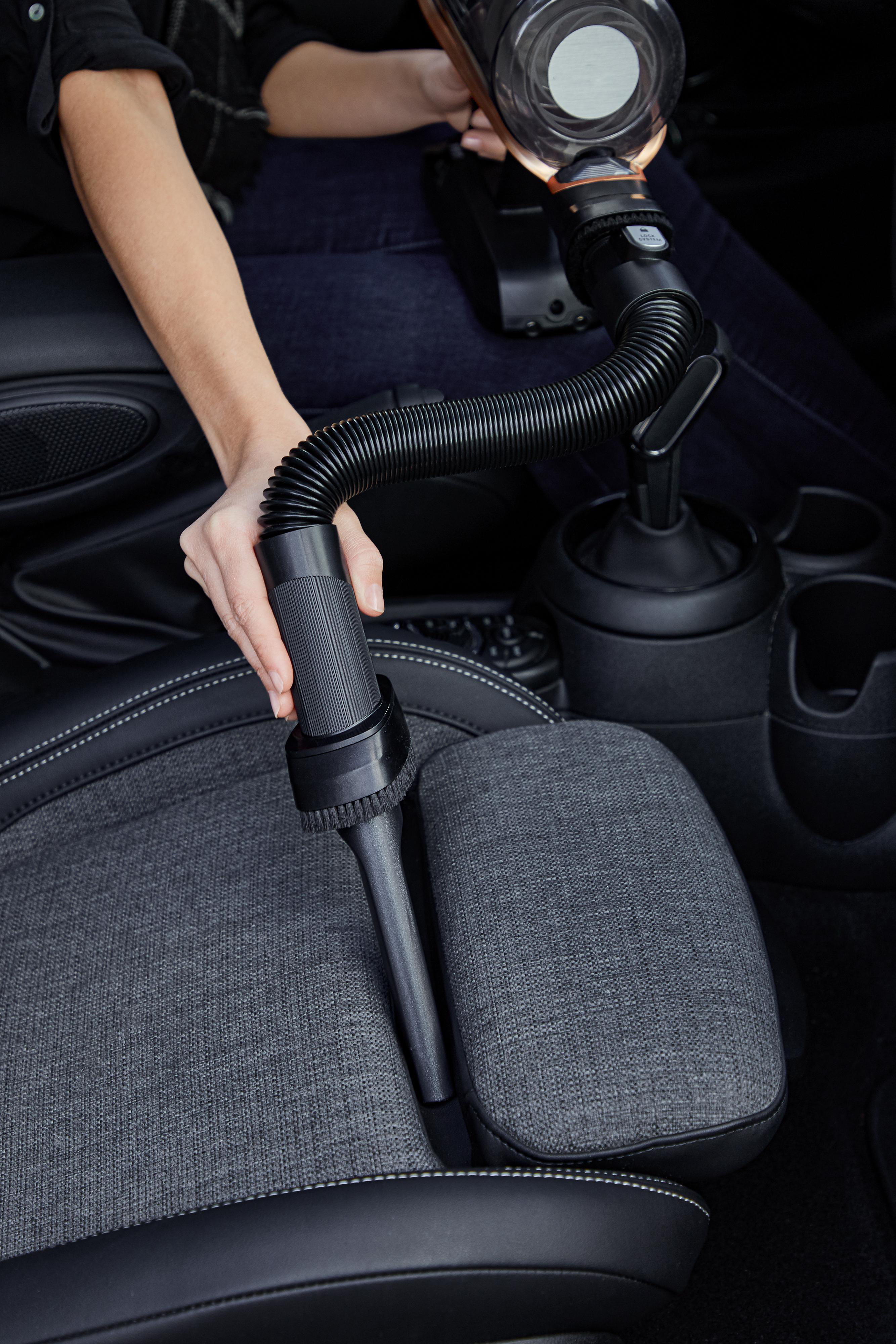 Person benutzt einen Handstaubsauger im Auto. Schwarzer und grauer Innenraum.