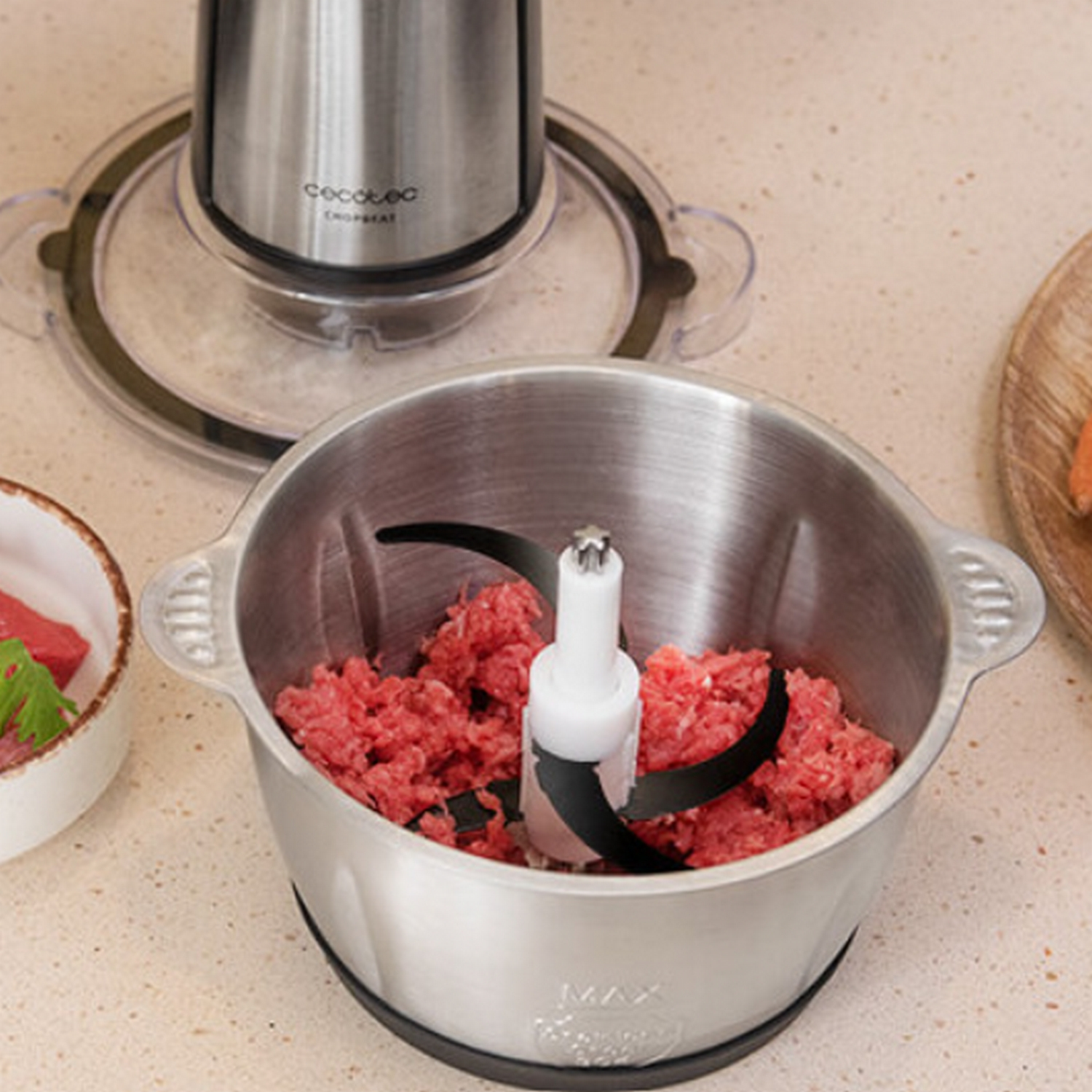 Un cuenco de procesador de alimentos de acero inoxidable con carne picada y cuchillas sobre una encimera.