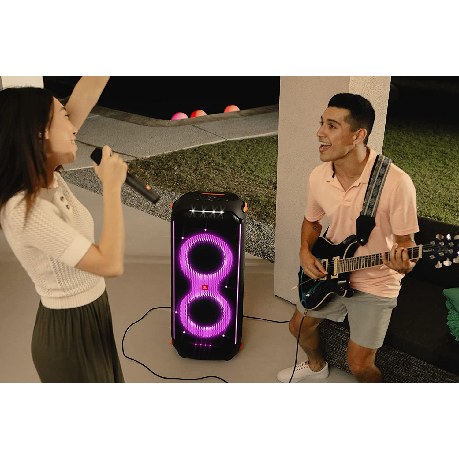 Dos personas cantan y tocan la guitarra junto a un altavoz con luces. Escena nocturna.