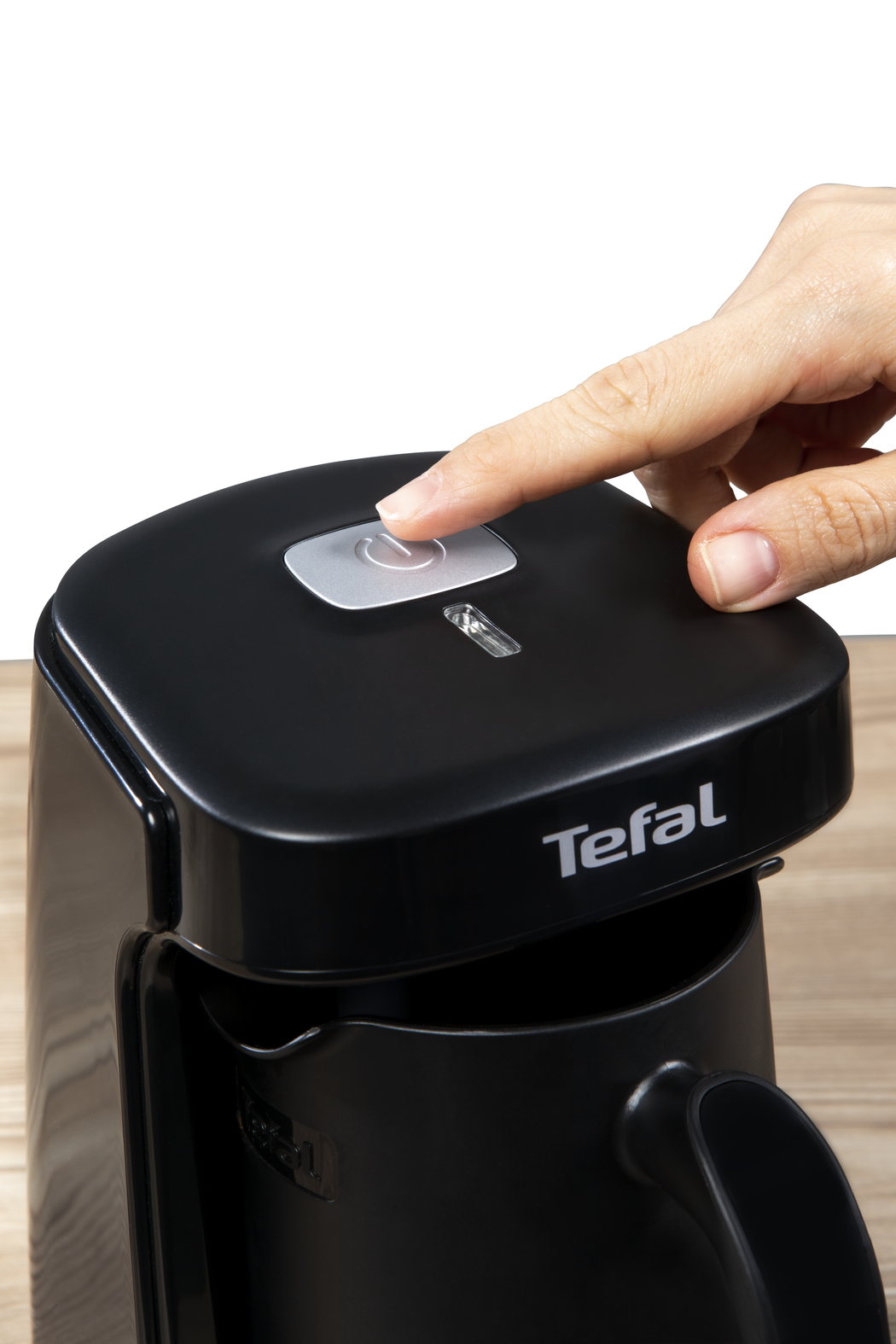 Bir el, siyah bir Tefal kahve makinesinin düğmesine basıyor. Güç düğmesi yanıyor.