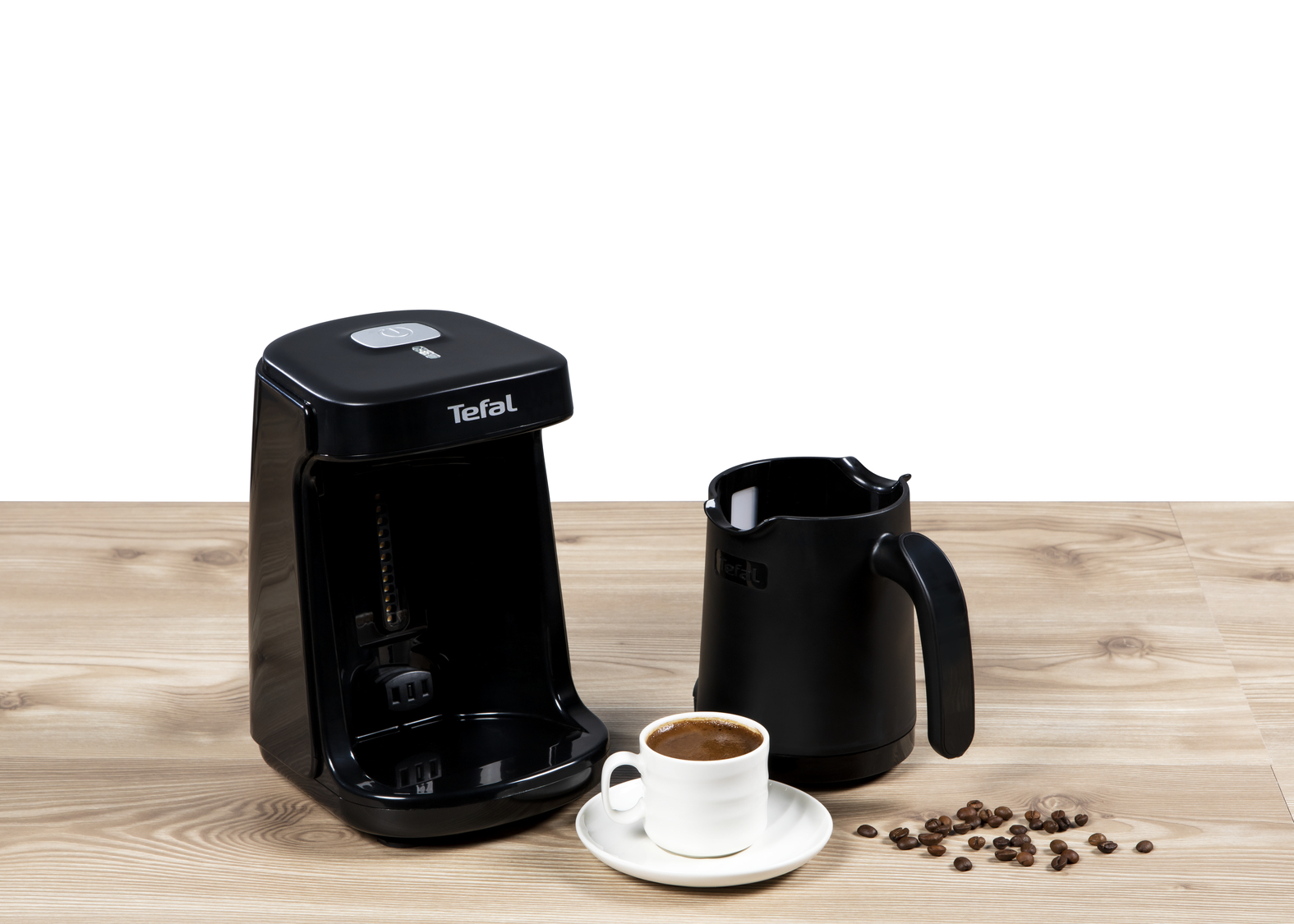 Siyah Tefal kahve makinesi, bir fincan kahve, kahve çekirdekleri ve ahşap üzerinde siyah bir kahve demliği ile.