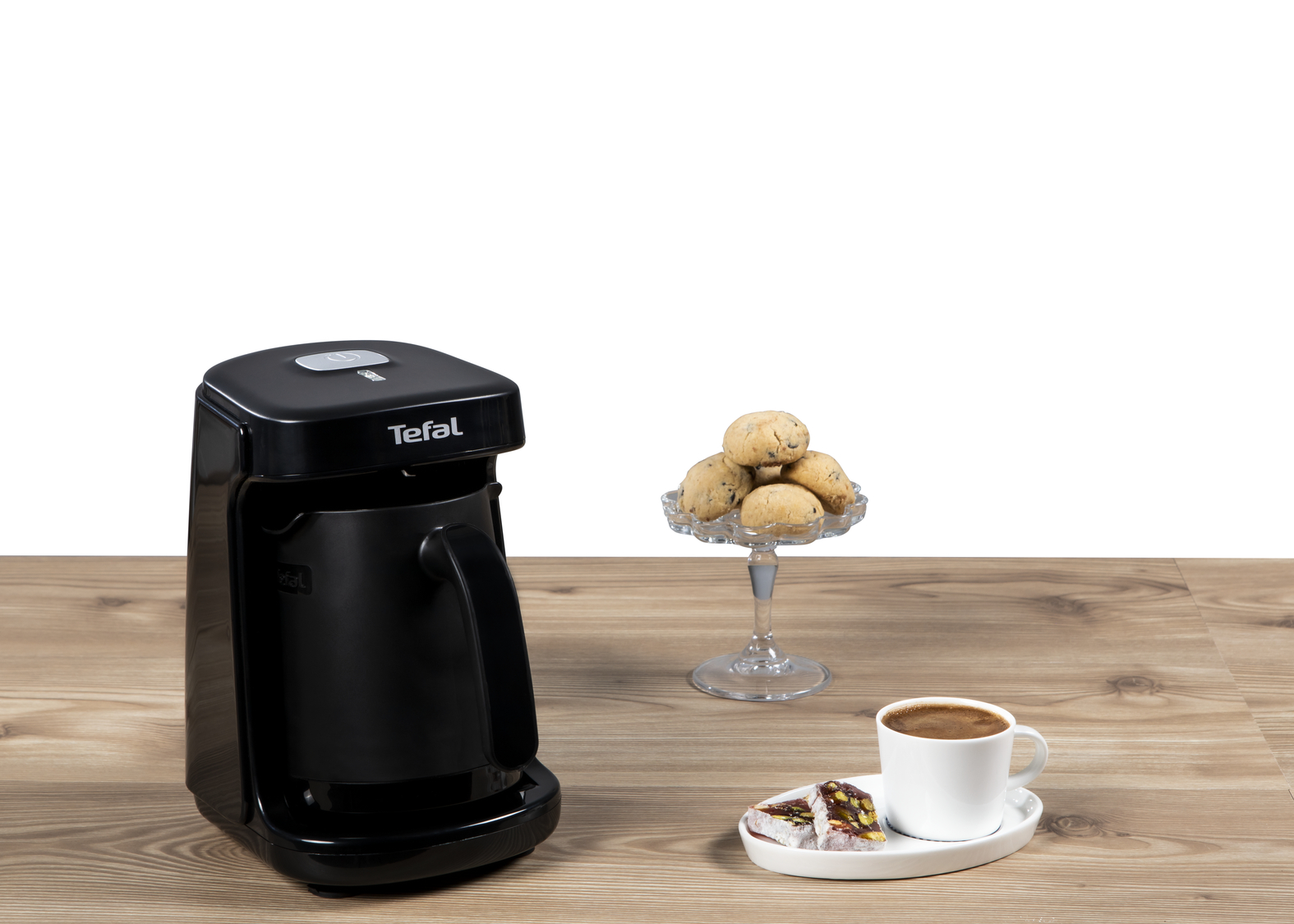 Siyah Tefal kahve makinesi, kurabiyeler ve bir fincan kahve ile bir masada.