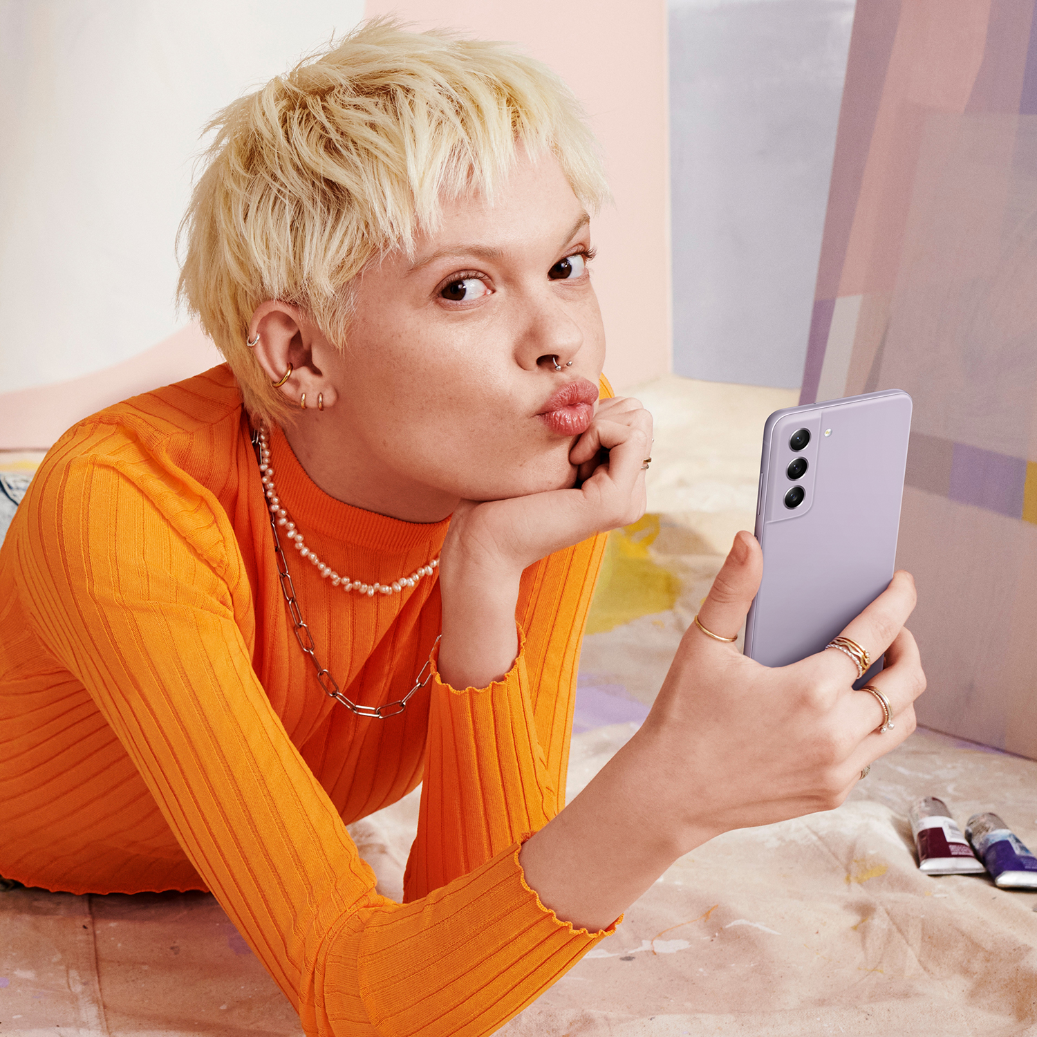 Mujer rubia sosteniendo un teléfono morado, haciendo un beso, sobre un fondo colorido.