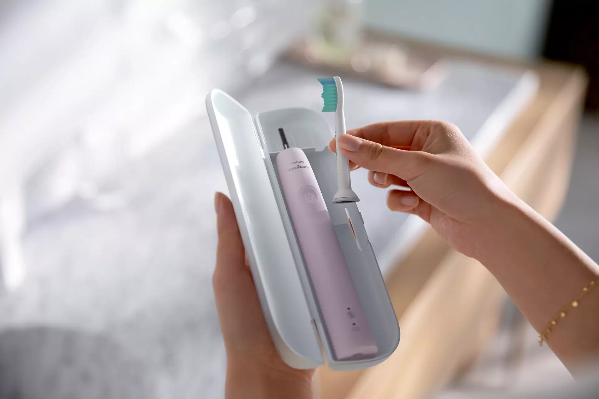 Une personne tient une brosse à dents électrique rose de son étui, avec une tête de brosse à dents.