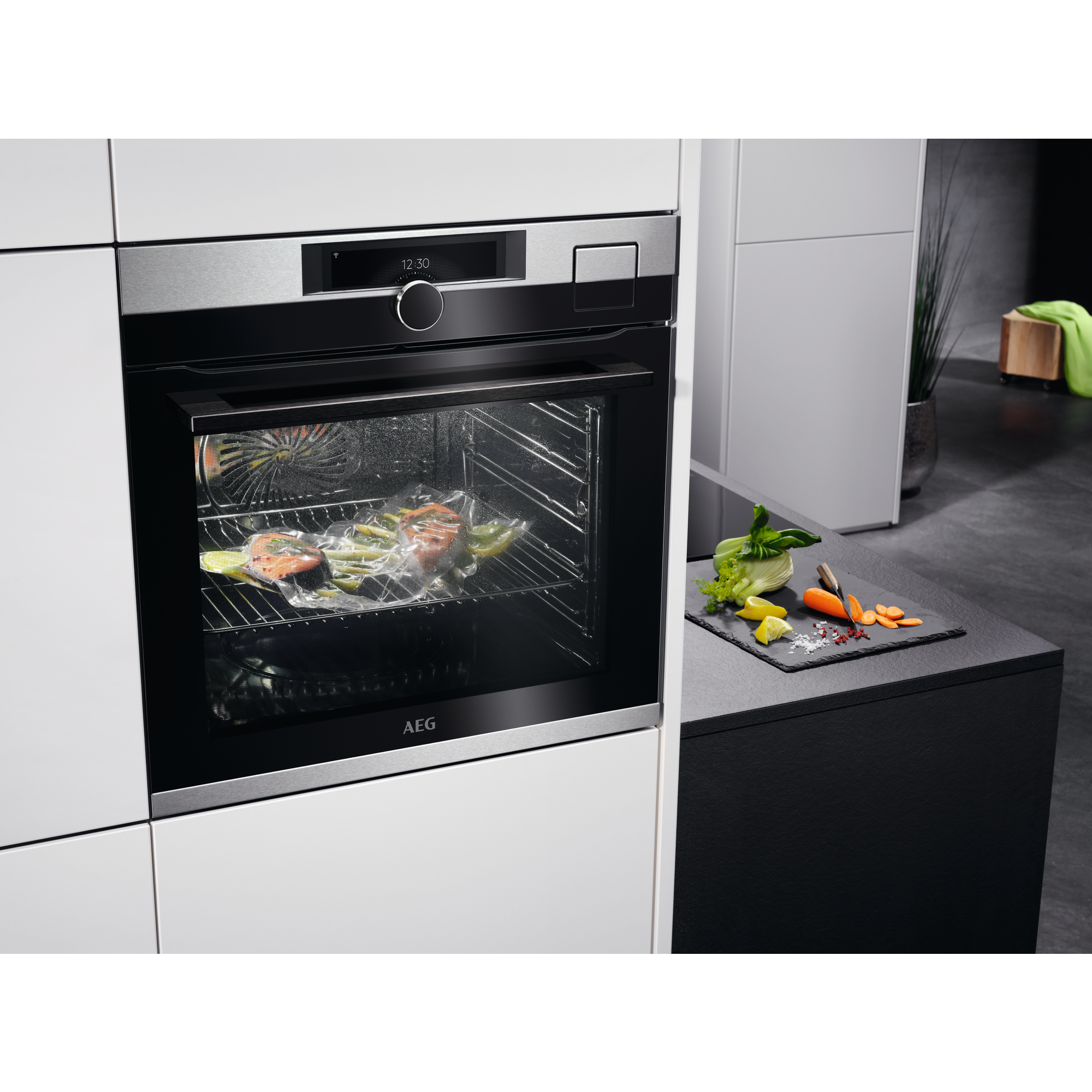 Ein Backofen mit geöffneter Tür. Im Inneren befinden sich versiegelte Lebensmitteltüten. Ein Schneidebrett mit Gemüse liegt daneben.