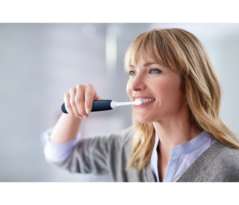 A woman is brushing her teeth with a toothbrush in front of a mirror.