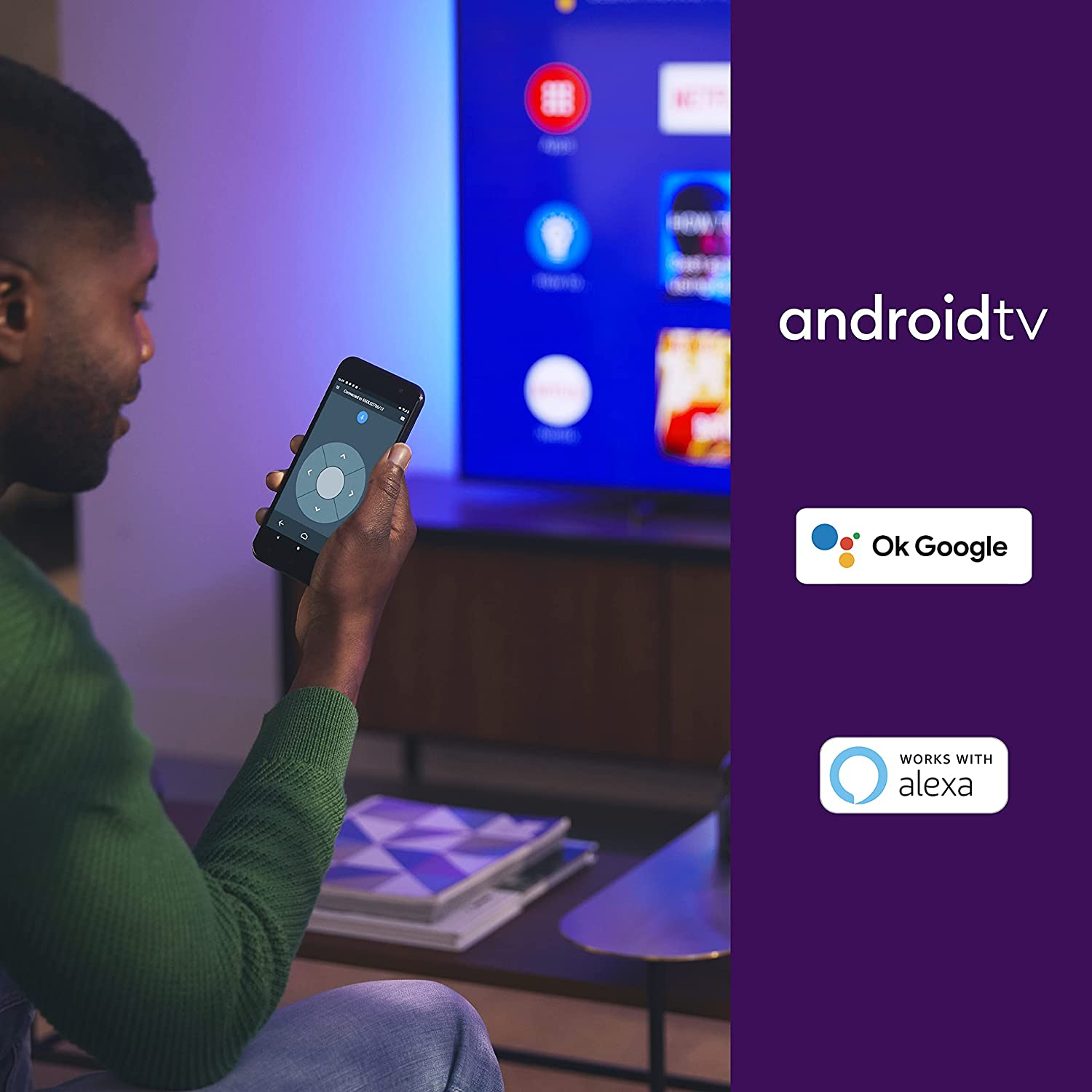 Un hombre sosteniendo un teléfono inteligente, mirando una pantalla de televisión.