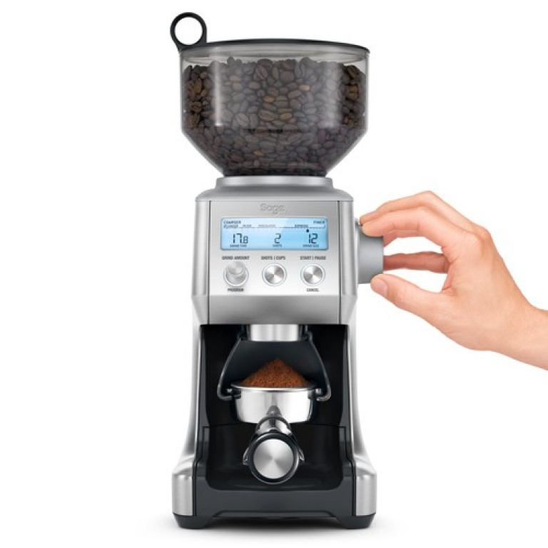 Zilveren koffiemolen met bonenreservoir en digitaal display, een hand stelt de molen in.