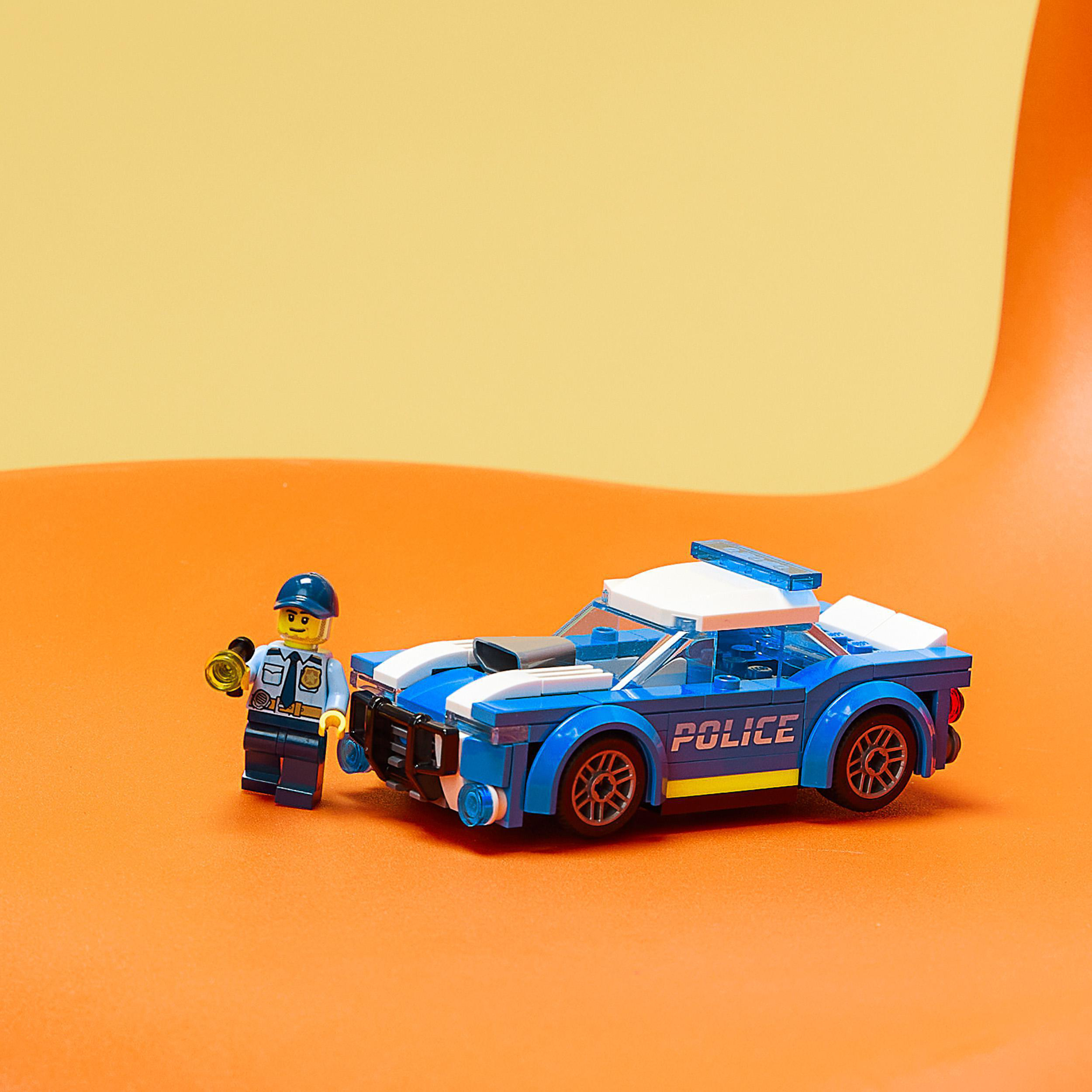 Ein Lego-Polizeiauto und ein Lego-Polizist auf orangefarbener Oberfläche mit gelbem Hintergrund.