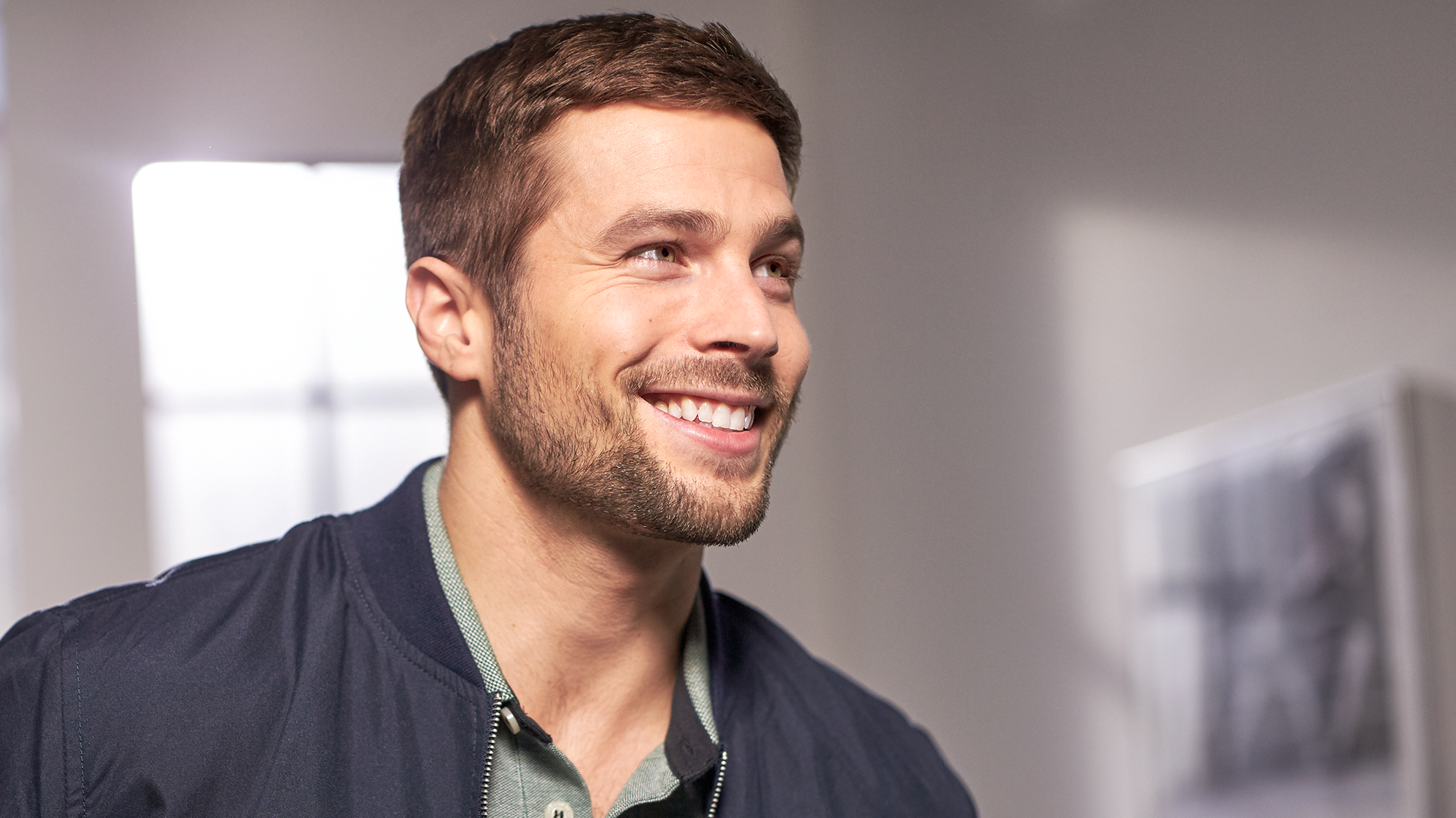 A smiling man in a dark jacket is looking to the right.