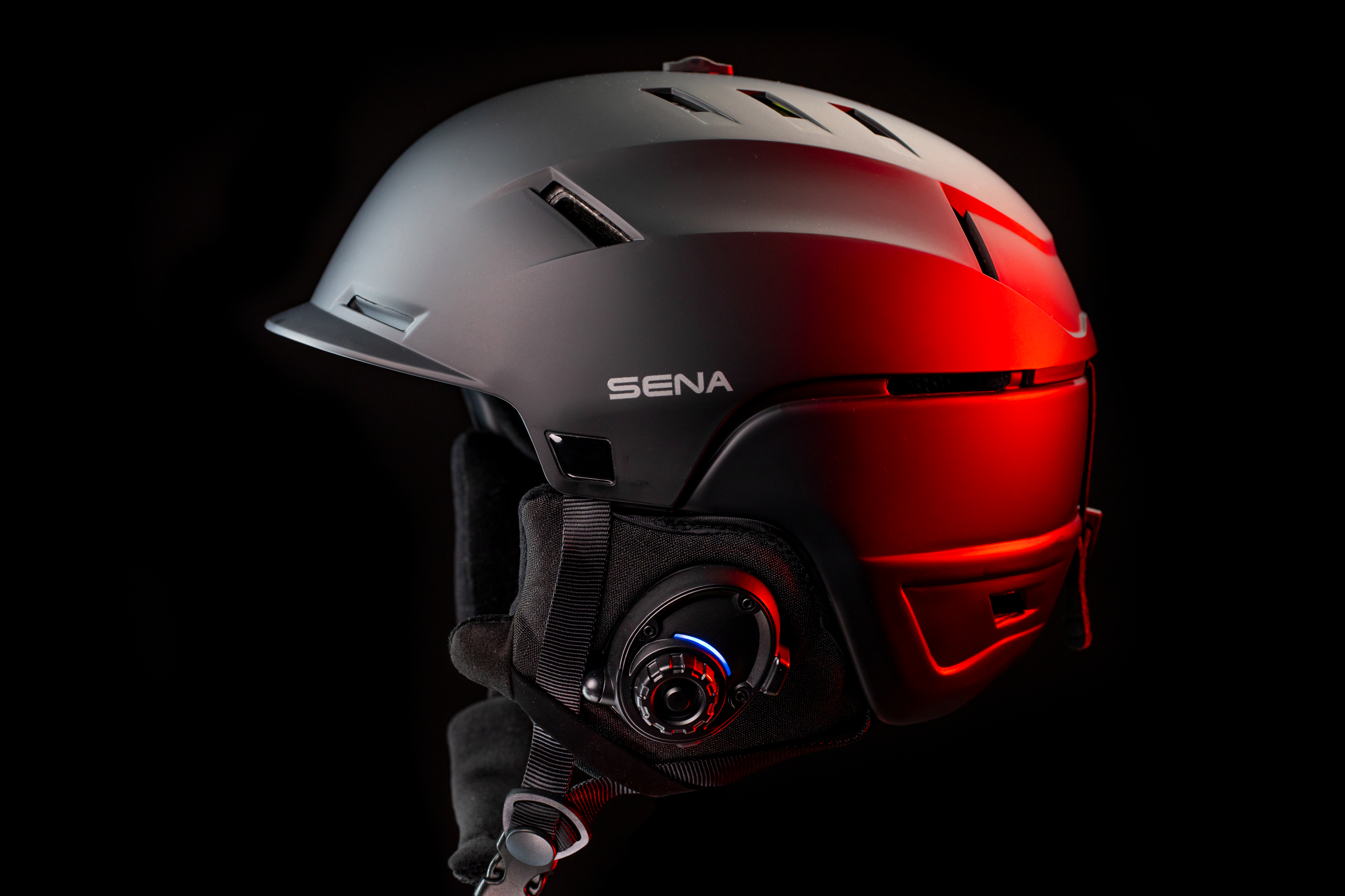 Schwarzer Skihelm mit Sena-Logo auf schwarzem Grund, rot beleuchtet.