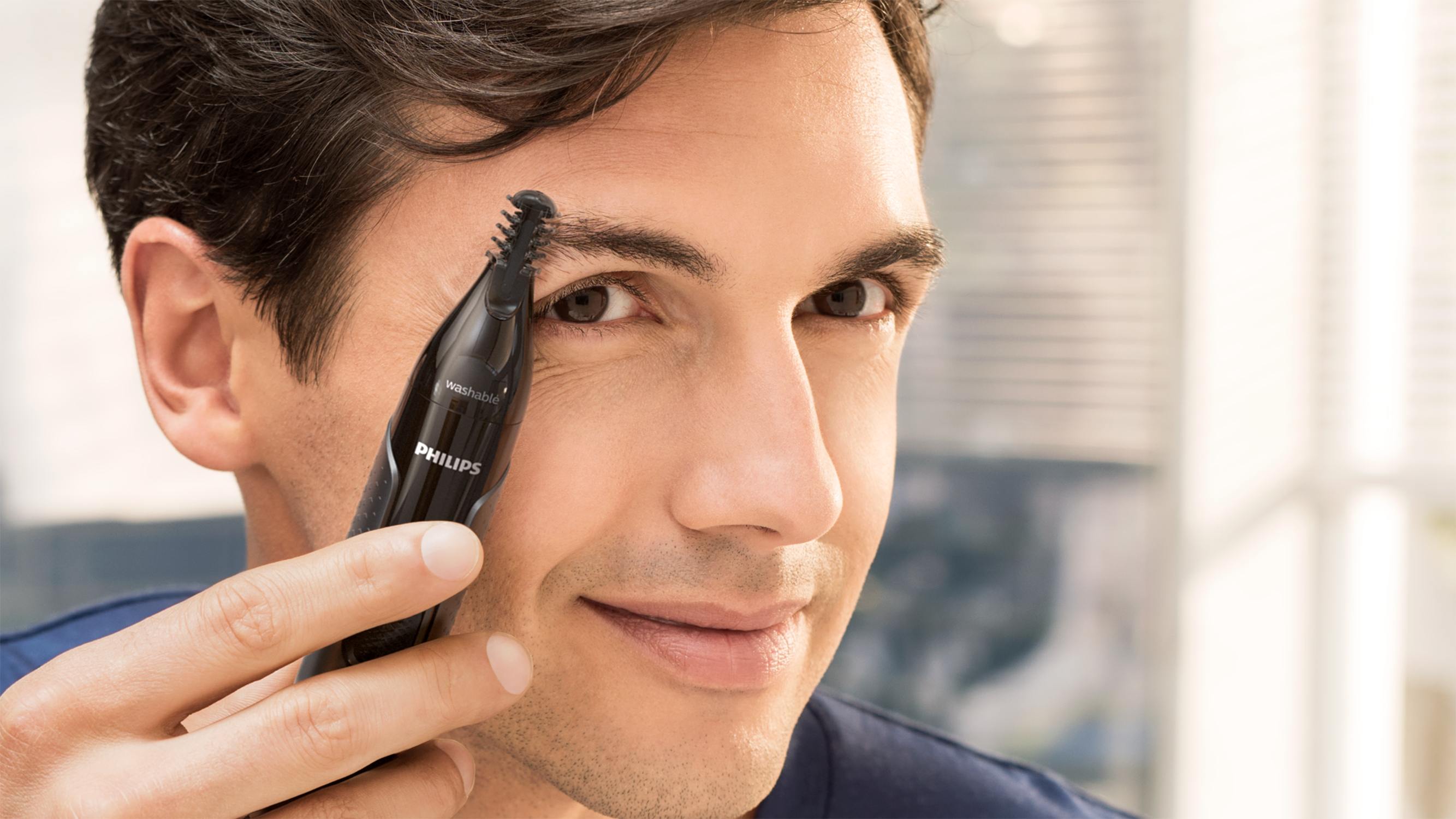 Man using a Philips nose trimmer.  He is smiling.
