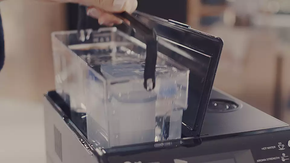 A person is adding water to a transparent water tank of a black coffee machine.