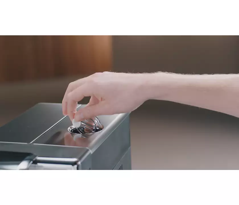 A hand inserting a capsule into a black coffee machine. The background is blurred.