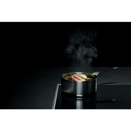 Een roestvrijstalen steelpan met eten erin, stoomt, op een zwart fornuis. Zwarte achtergrond.