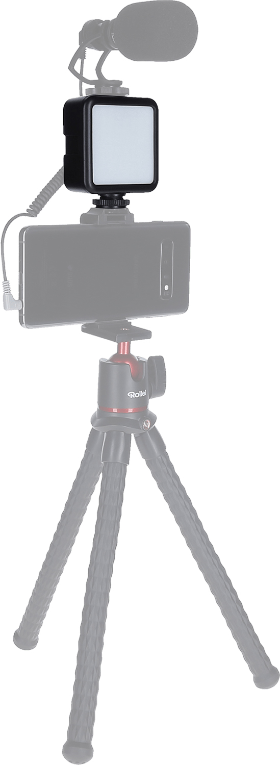 Un smartphone avec une lumière et un microphone attachés est posé sur un trépied. Des couleurs noires et rouges sont présentes.