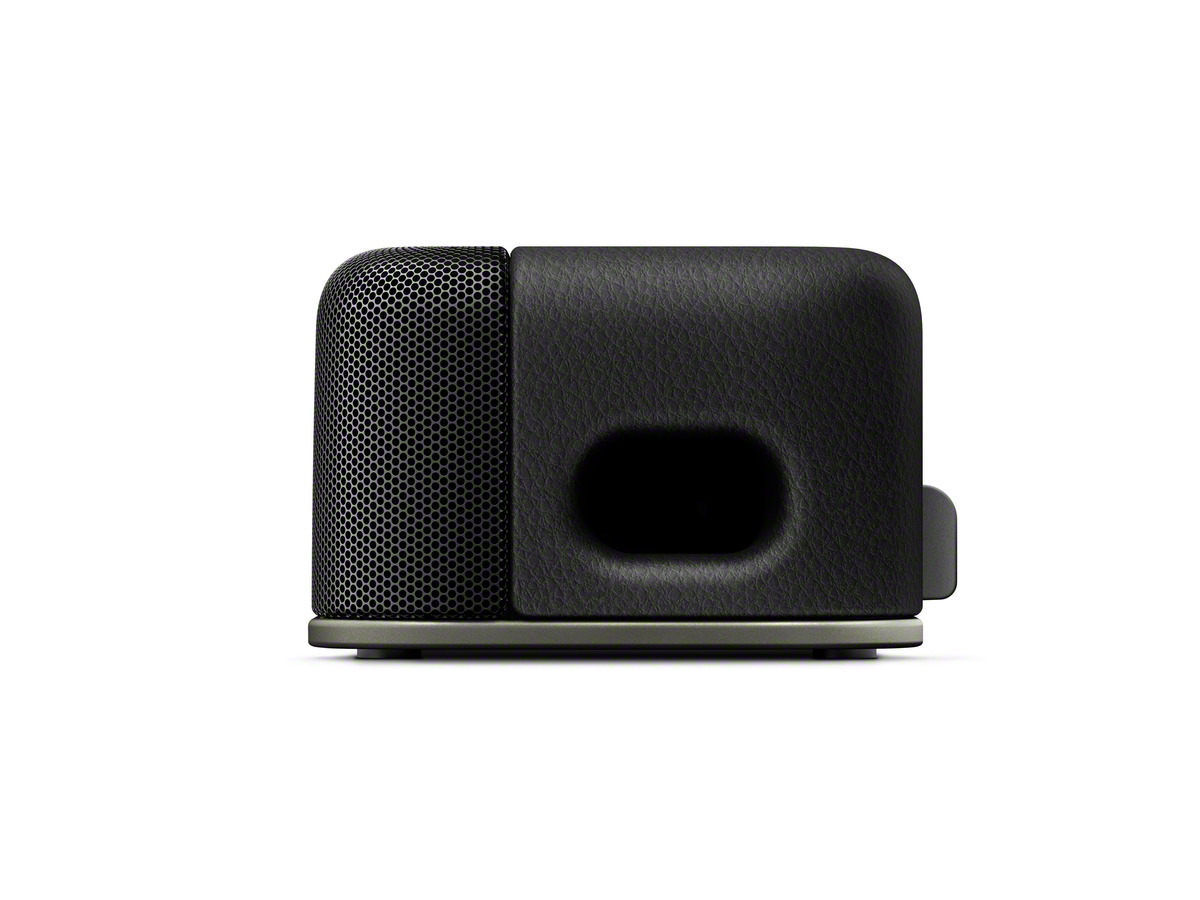 Un altavoz negro sobre un fondo blanco. El altavoz tiene una parte frontal de malla y una parte trasera lisa, similar al cuero.