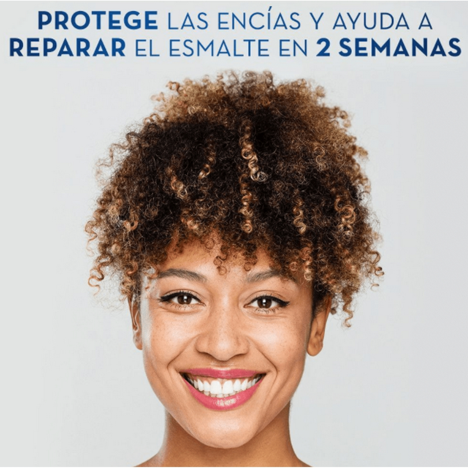Una mujer sonriente con cabello rizado, mostrando dientes blancos, con texto sobre protección de encías y reparación de esmalte.