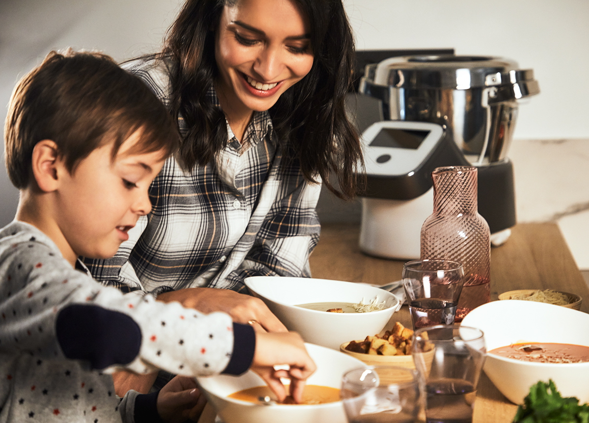 Une mère et son enfant cuisinent de la soupe ensemble. Des équipements de cuisine et des bols sont visibles.