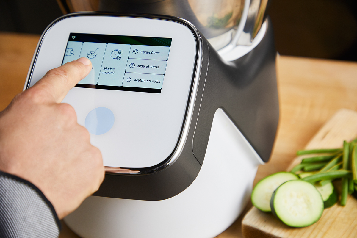 Main touchant l'écran d'un appareil de cuisine, avec options de cuisson affichées.