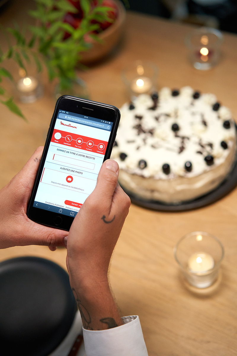 Une personne tenant un téléphone avec une application ouverte, un gâteau et des bougies sur une table.