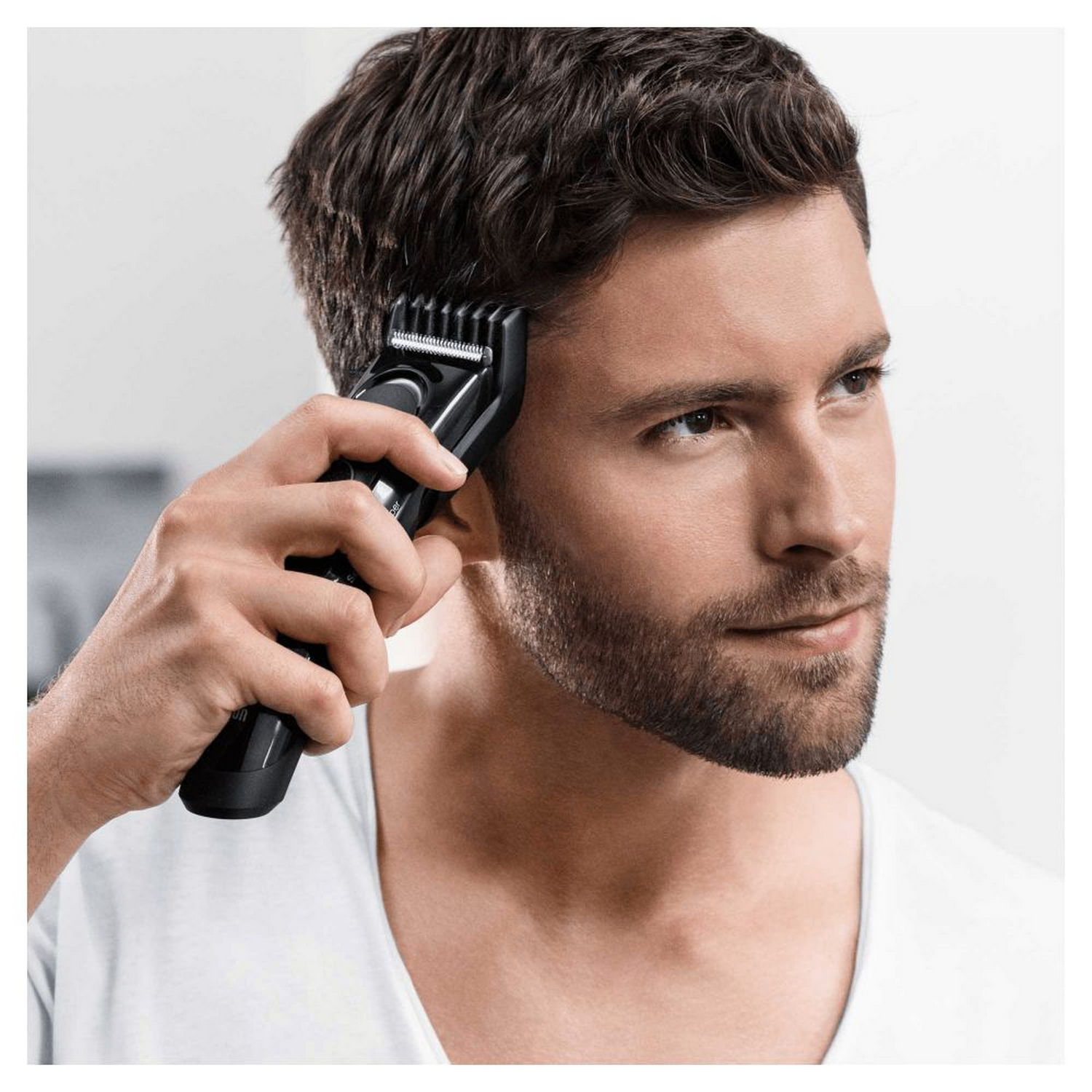 Hombre usando un cortapelos negro, recortando el cabello cerca de su oreja.