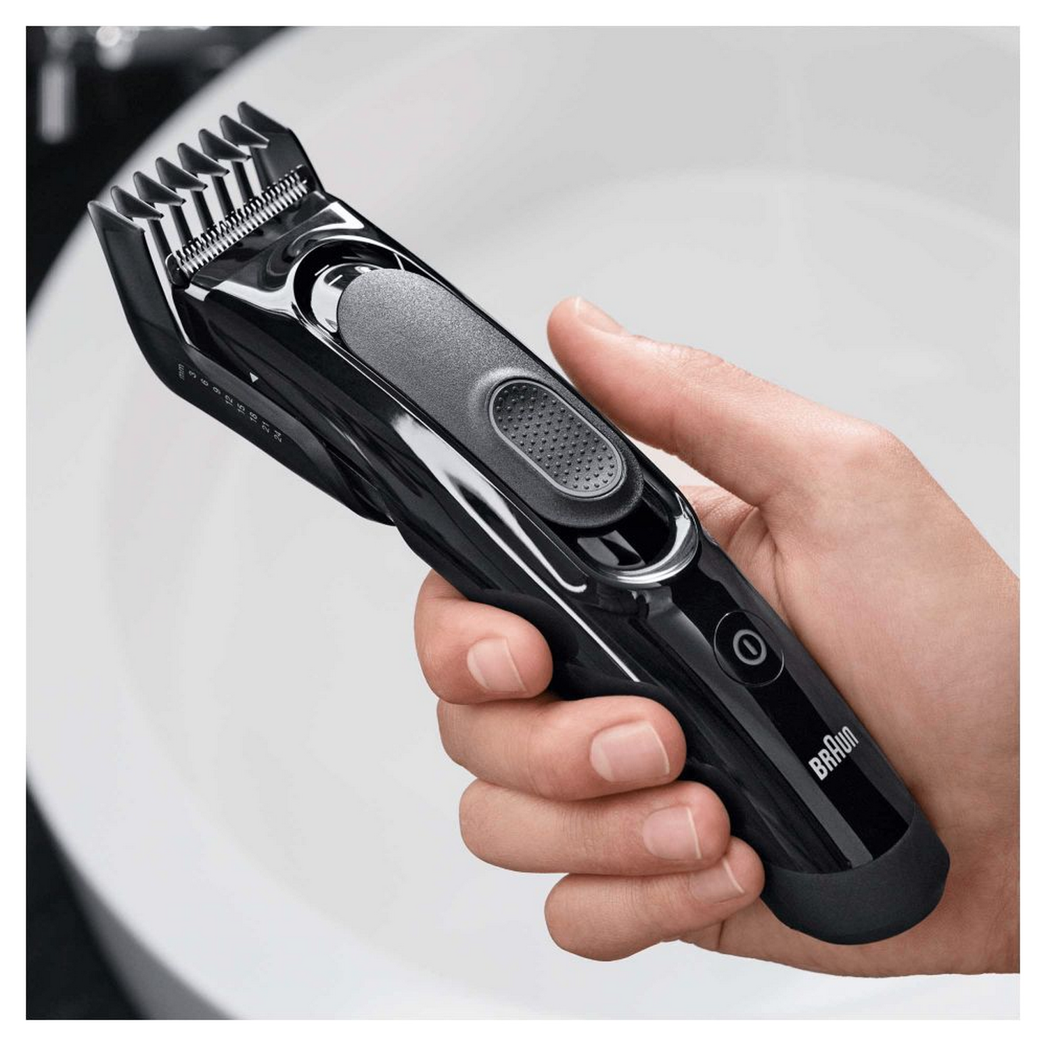 Una recortadora de barba Braun negra sostenida en una mano, con fondo blanco.