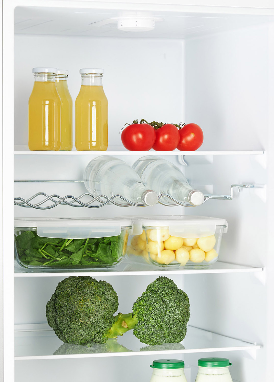 A refrigerator with shelves containing bottles of juice, tomatoes, and vegetables in containers.