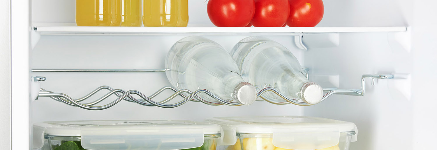 Close up of refrigerator shelves. Bottles of water, containers with food and red tomatoes are present.