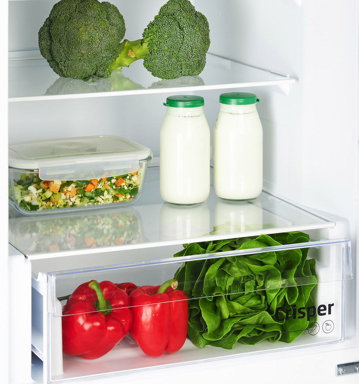Inside refrigerator with vegetables: broccoli, lettuce, red peppers, milk bottles, and a glass container.