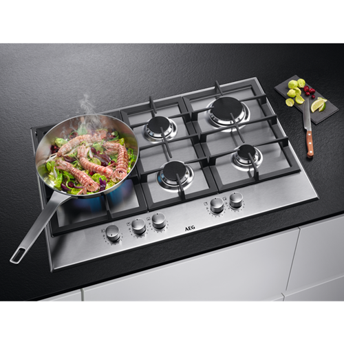 Roestvrijstalen gasfornuis. Pan met eten dat kookt. Zwart aanrecht. Groenten en mes.