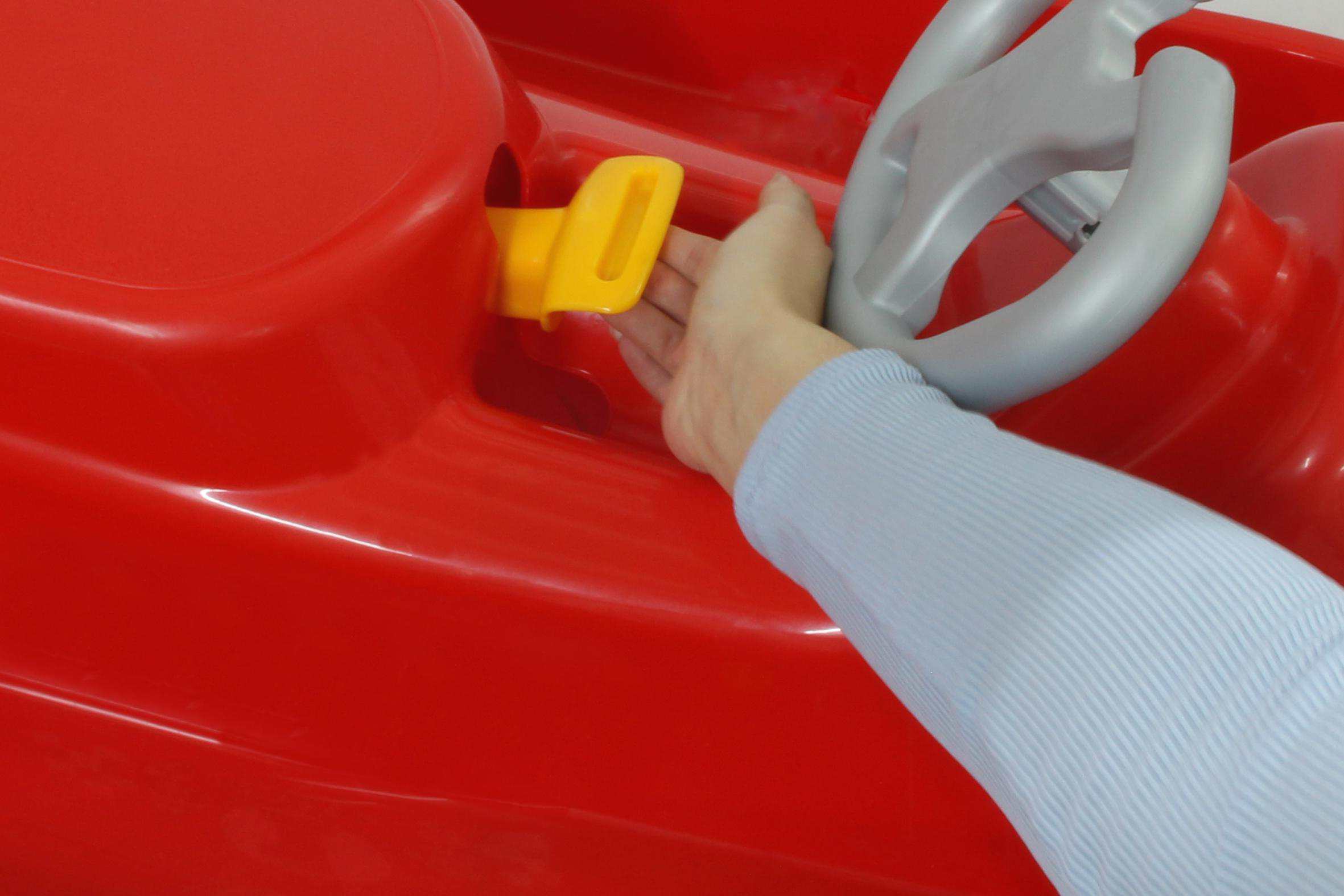 Eine Hand stellt einen gelben Hebel an einem roten Spielzeugauto ein. Das Auto hat ein graues Lenkrad.