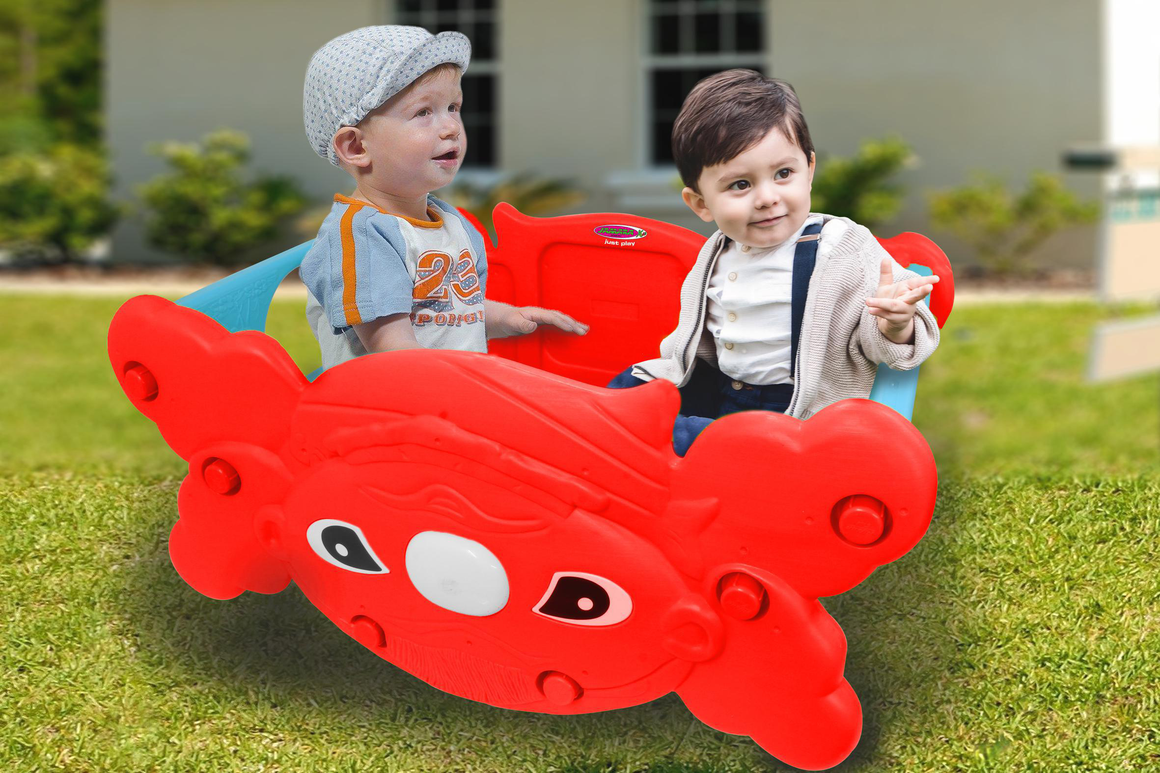 Zwei Kinder in einem roten krabbenförmigen Spielzeug auf einer Wiese.