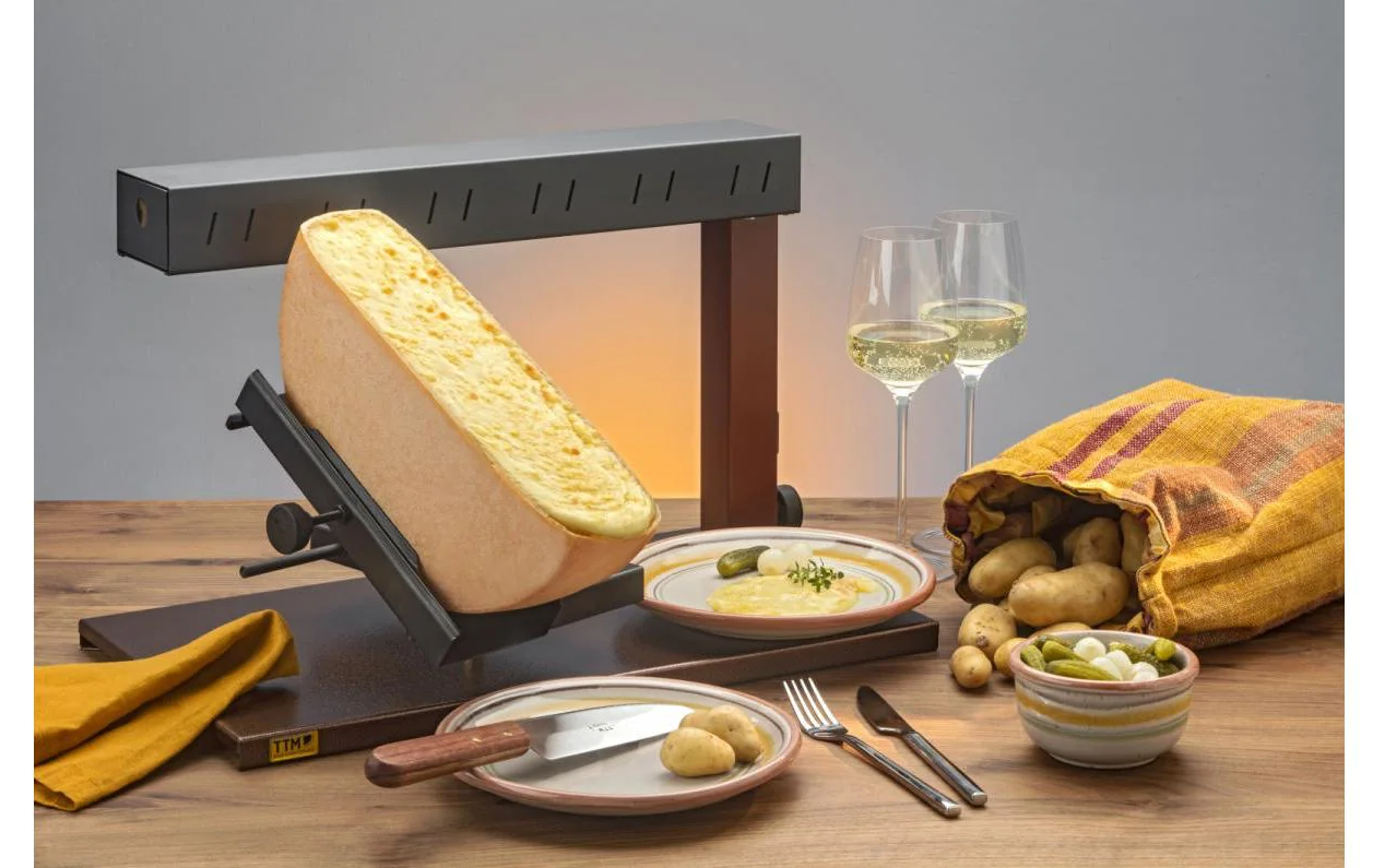 Raclette-Set mit Käse, Kartoffeln, Essiggurken und Weingläsern.