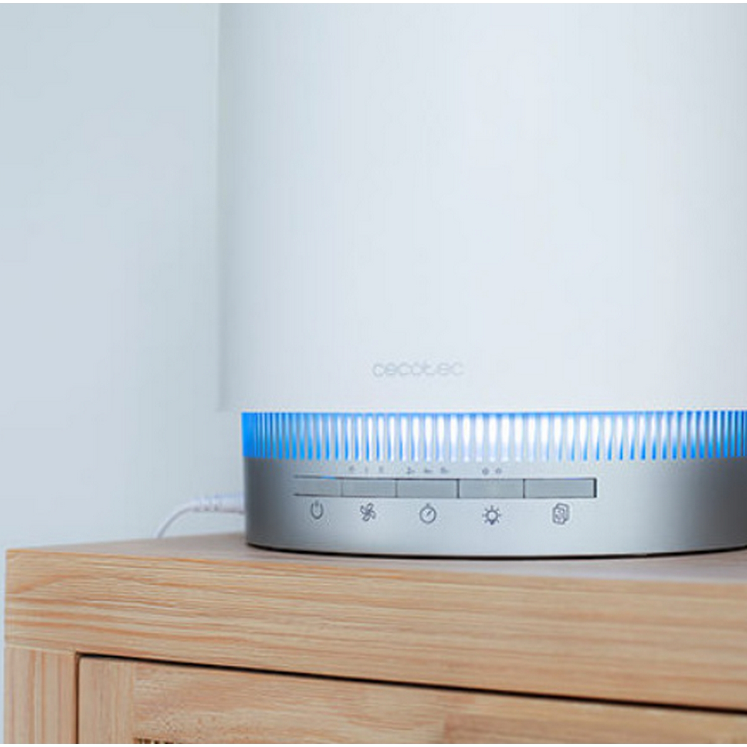 Un purificador de aire blanco sobre una superficie de madera. Tiene luces azules y botones de control. El fondo es blanco.