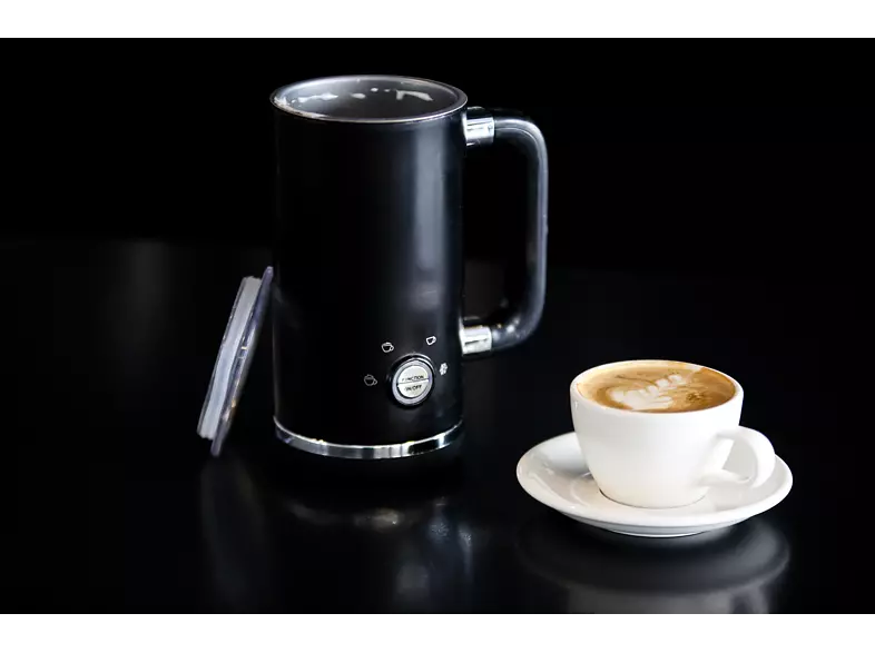 A black milk frother with a handle, and a cup of coffee with latte art on a black surface.
