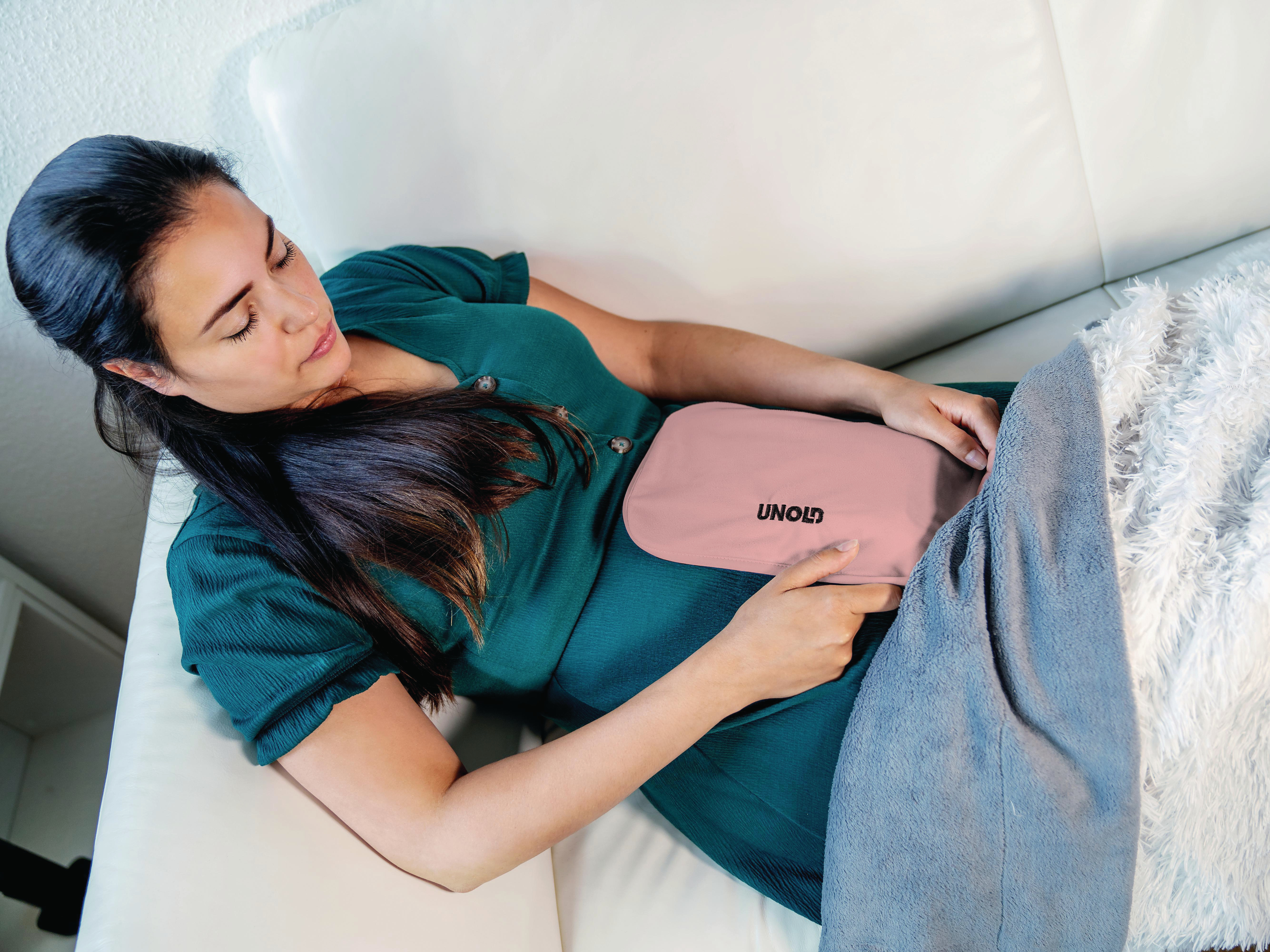 Frau auf weißem Sofa mit rosa Wärmepack am Bauch.